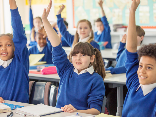 Group of school children wearing blue uniform with hands up in air