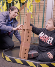 A practitioner sits with a pupil playing with bricks.