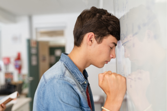 Young man with head against wall and clenched fist looking distressed