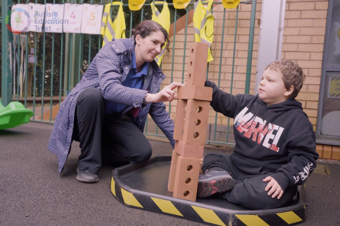 A child and practitioner sit outside playing with bricks